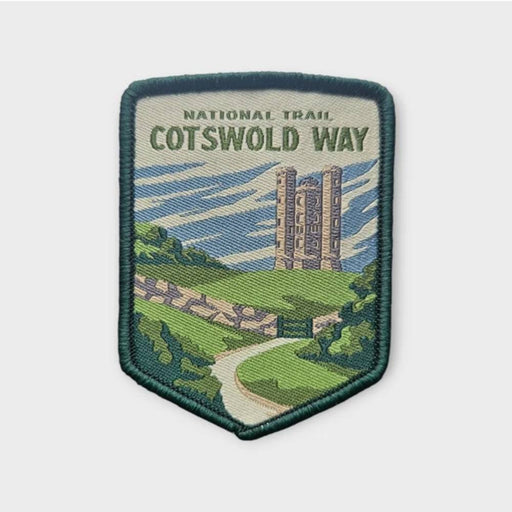 An embroidered patch for the National Trail Cotswold Way, featuring a scenic illustration of a stone tower, green fields, and a winding path under a blue sky, with a dark green stitched border.