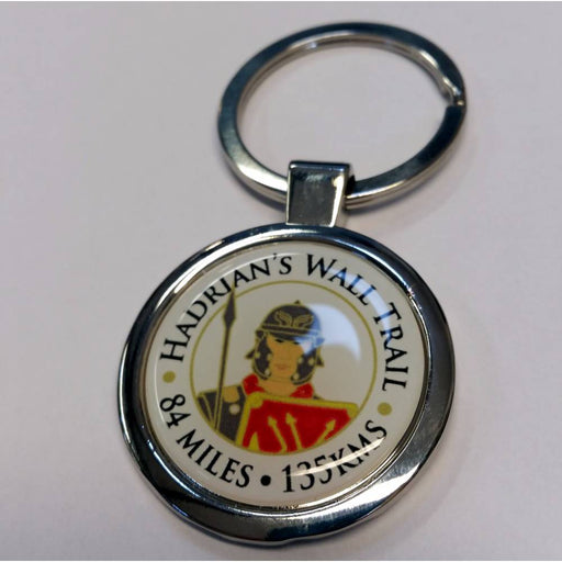 A round metal keychain featuring a glossy emblem with the text 'HADRIAN'S WALL TRAIL 84 MILES 155 KMS' and an illustration of a Roman soldier, attached to a silver split ring on a light background.