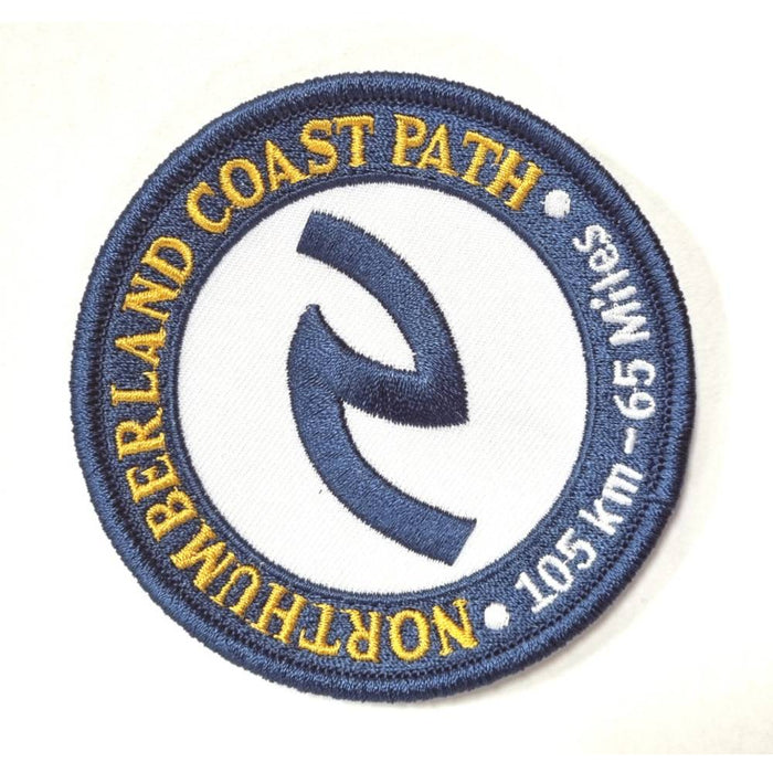 A circular embroidered patch for the Northumberland Coast Path, featuring a navy blue border and central symbol on a white background with yellow and white text.
