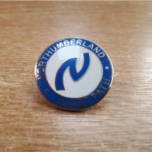 Northumberland Coast Path enamel badge on a wooden surface