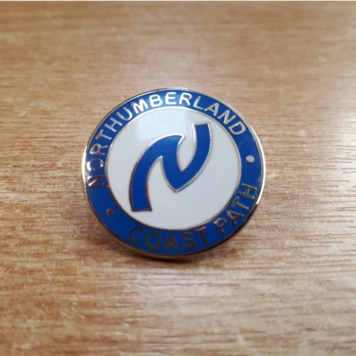 Northumberland Coast Path enamel badge on a wooden surface